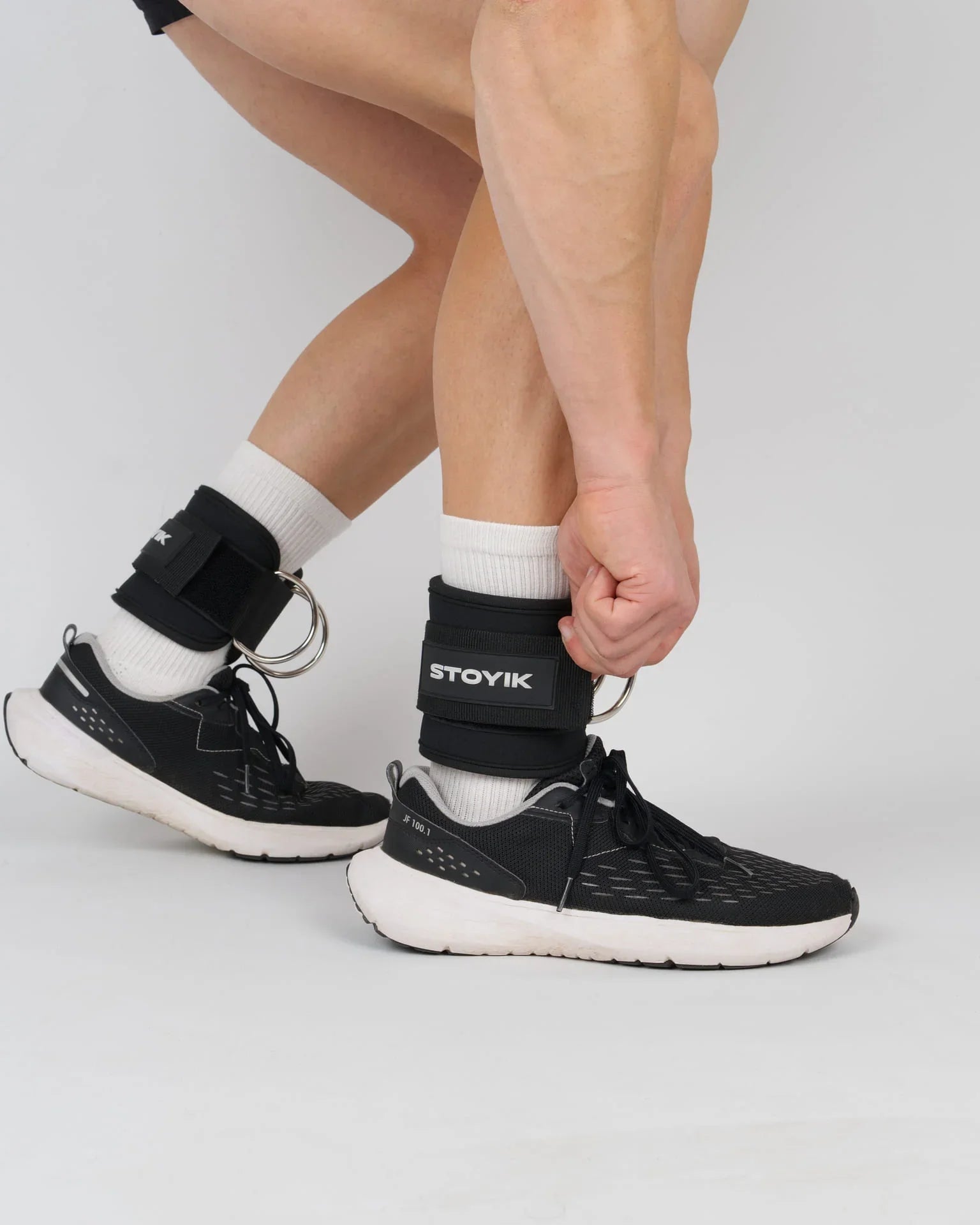 Athlète ajustant les sangles de cheville STOYIK noires sur ses jambes avant un exercice de tirage ou de fessiers