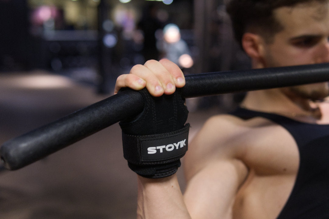 Gros plan sur des mains gantées tenant une barre de musculation avec des sangles de tirage STOYIK Athletics pour améliorer la prise