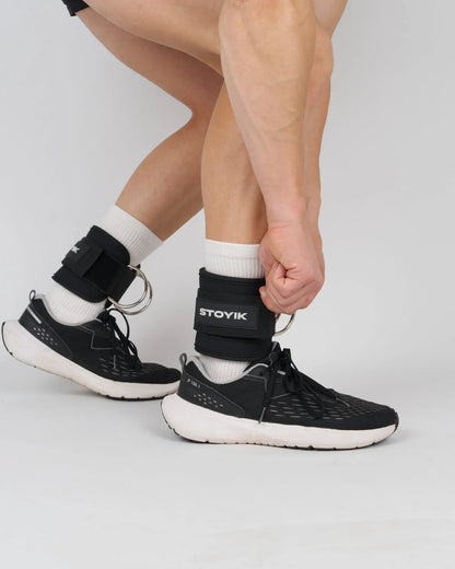 Athlète ajustant les sangles de cheville STOYIK noires sur ses jambes avant un exercice de tirage ou de fessiers